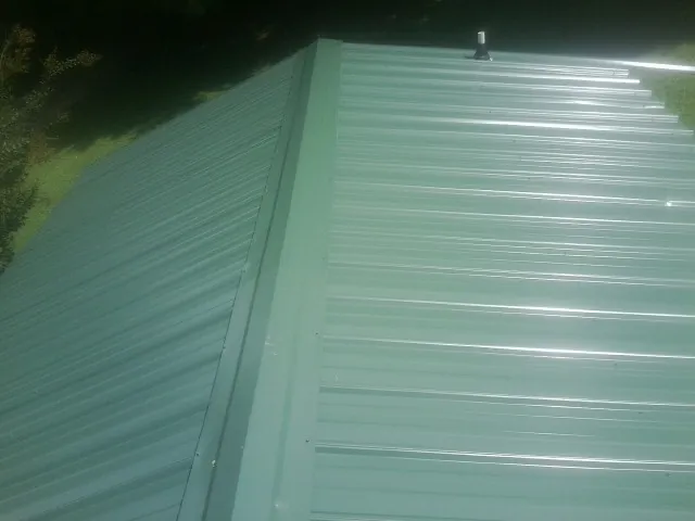New green metal panels meeting at the ridge of a roof — Flat Roof Repair work by our crew in Smyrna