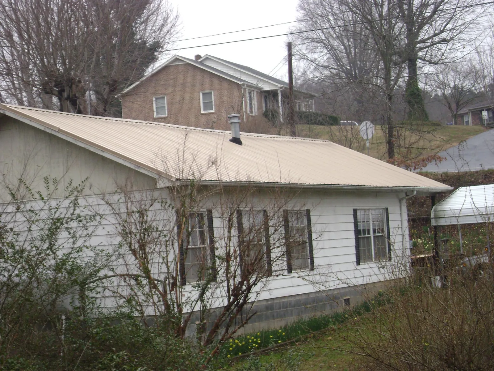 Tan metal roof on a white sided house set into a hillside — Commercial Roofing by Roofing Brothers in Smyrna